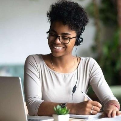 Woman smiles while writing and using laptop